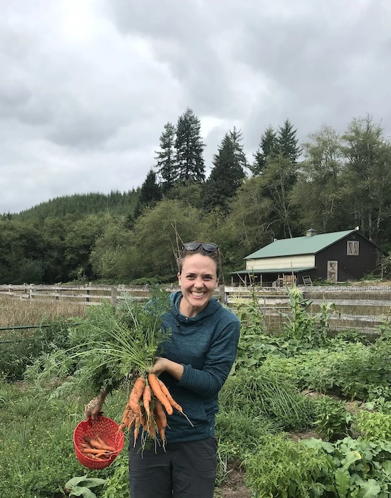 Megan holding up freshly harvested carrots in her garden.